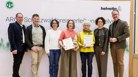 Gruppe von sieben Personen mit Auszeichnungen vor einem Hintergrund mit Logos.