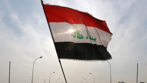 Grosse Flagge mit rotem, weissem und schwarzem Streifen weht im Wind unter blauem Himmel.