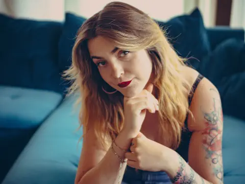Frau mit langen Haaren und Tattoos auf blauem Sofa.