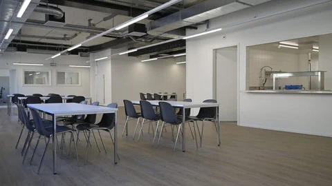 Moderner Speisesaal mit weissen Tischen und schwarzen Stühlen.