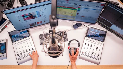 Radiostudio mit Mischpult, Mikrofon und Bildschirmen.