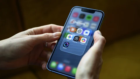 Hände halten ein Smartphone mit geöffnetem Ordner für Chatbot-Apps.
