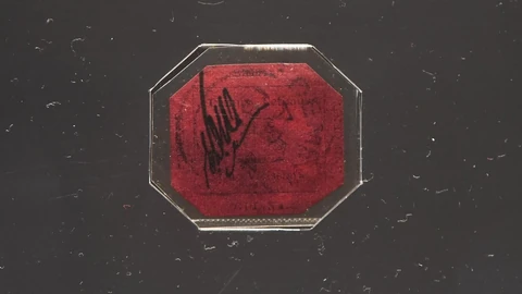 Rote Briefmarke mit schwarzem Aufdruck in achteckigem Rahmen.