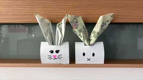 Zwei Papierhasen mit bemalten Gesichtern auf einem Regal.