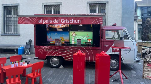 Roter Lieferwagen mit Aufschrift 'al puls dal Grischun' und aufgebautem Infostand.