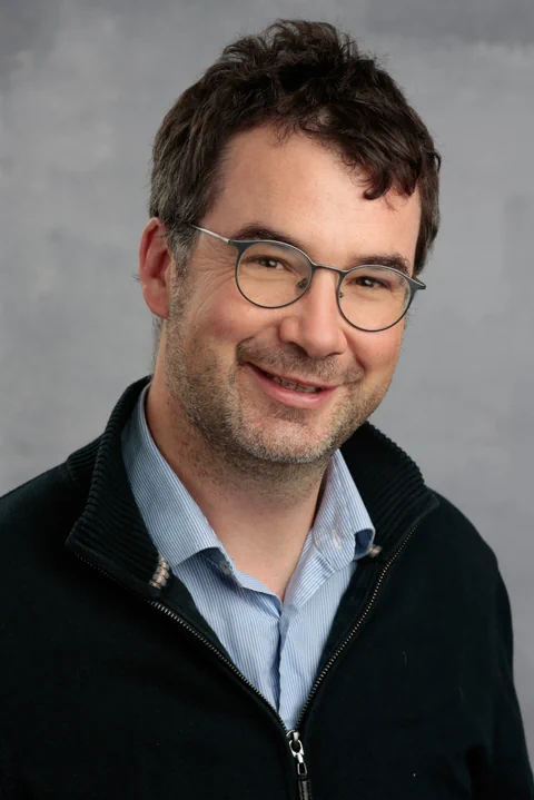 Porträt eines lächelnden Mannes mit Brille und schwarzer Jacke