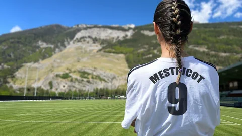 Frau im Fussballtrikot auf Fussballfeld mit Bergkulisse.