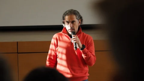 Mann in rotem Pullover hält Mikrofon und spricht.