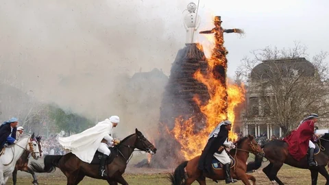 Reiter in traditionellen Gewändern vor brennendem Stapel mit Figur.