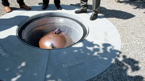 Mehrere Personen stehen um eine runde, in den Boden eingelassene metallische Struktur.