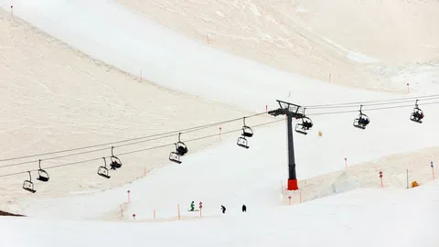 Schneebedeckter Hang mit Sessellift und Skifahrern.