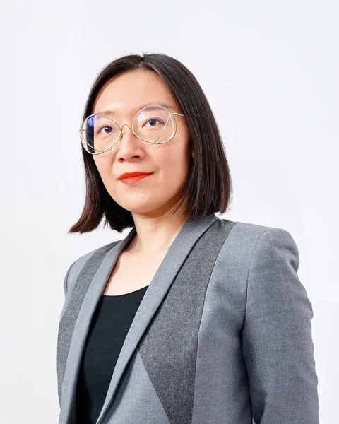 Frau mit Brille im grauen Blazer vor weissem Hintergrund.