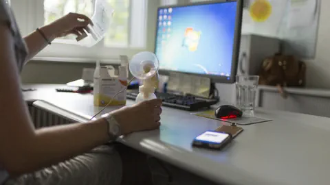 Person benutzt Milchpumpe am Schreibtisch mit Computer.