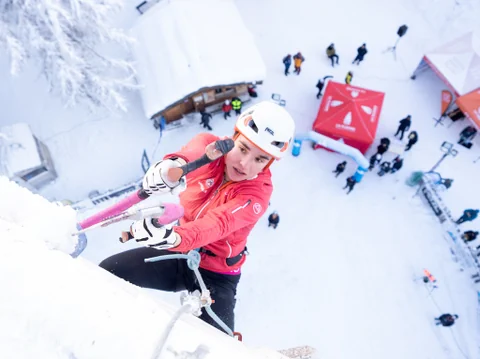 Frau klettert mit Eispickeln eine vereiste Wand hinauf.