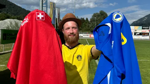 Mann mit Hut, der zwei Sporttrikots in einem Stadion hält.