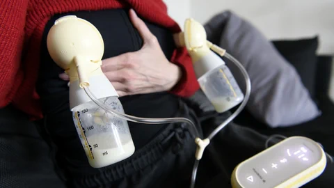 Person mit Brustpumpe und Milchflaschen.