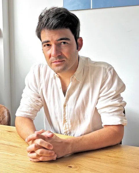 Person mit hellem Hemd sitzt an einem Holztisch.