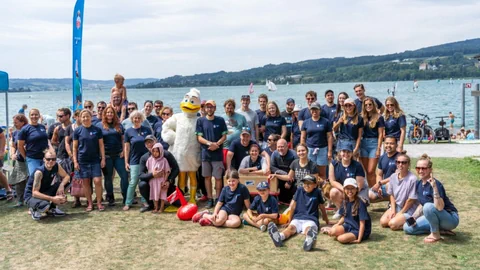 Gruppe von Menschen und Maskottchen an einem See versammelt.