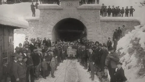 Menschenmenge vor einem Tunnelbauwerk im Schnee mit der Aufschrift '1903'.