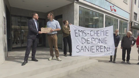 Gruppe hält Banner mit Aufschrift vor Bürogebäude.