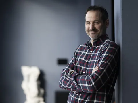 Mann in karriertem Hemd lehnt lächelnd an einer Wand.