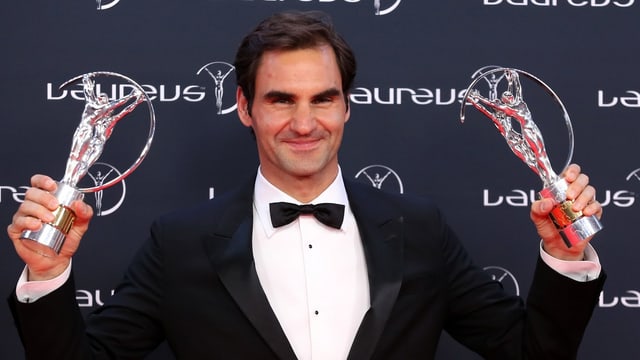 Purtret da Federer cun enta maun duas da las trofeas. 
