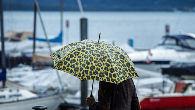 Ina persuna cun parasol a la riva dal Lago Maggiore.