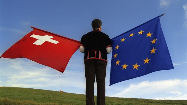 Maletg d'in svizzer che tegn la bandiera sivzra e quella da l'Uniun Europeica