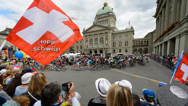 Aspectaturs dal Tour de Suisse e davos la gruppa dals velocipedists avant la Chasa federala. 