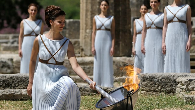 Ad Olimpia envida ina ballerina greca tradiziunala la flomma.