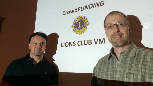 Patrick Wegmann e Plinio Meyer davant in screen cun si il logo dal Club da liuns.
