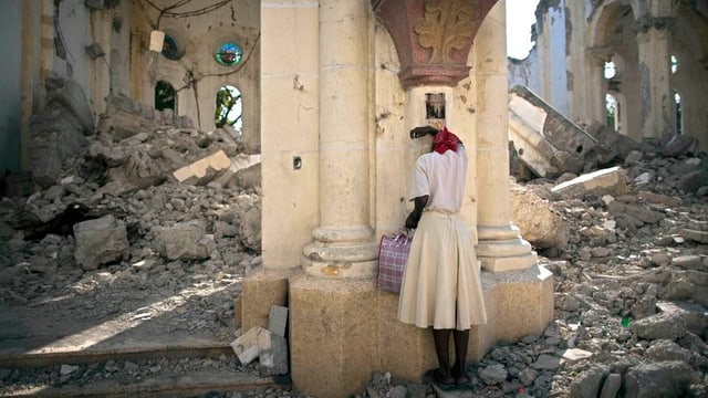 Ina dunna ura en las ruinas d’ina catedrala a Haiti.