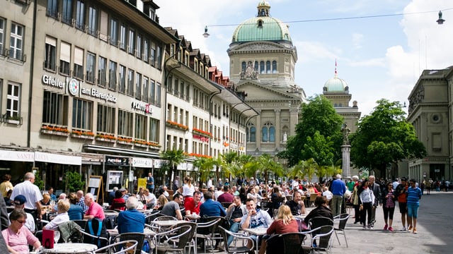Numerusas persunas sesan en in café sin il 'Bärenplatz' a Berna.