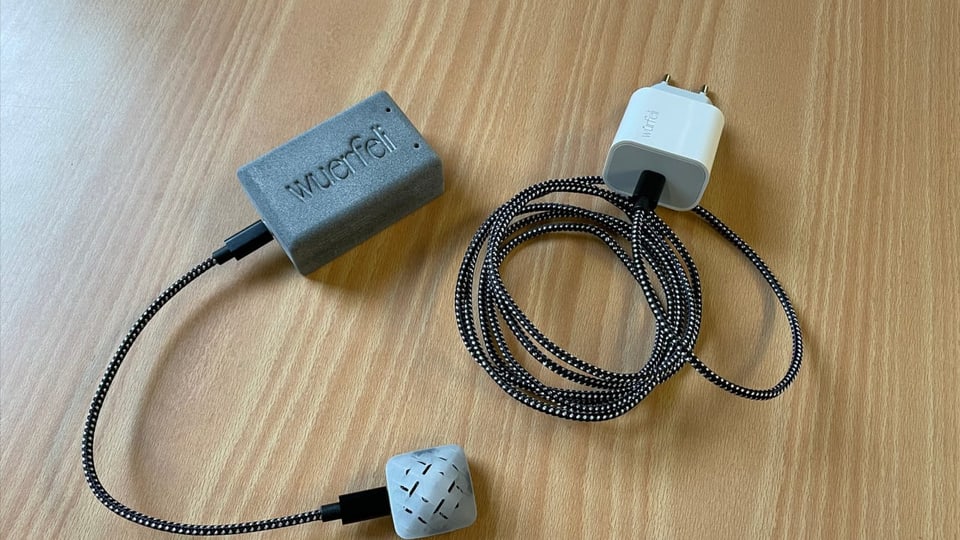 L'apparat che mesira la concentraziun da CO2 purtret d'in quaderin cun vidlunder in cabel che maina al toc che mesira ed in al toc per l'electricitad.