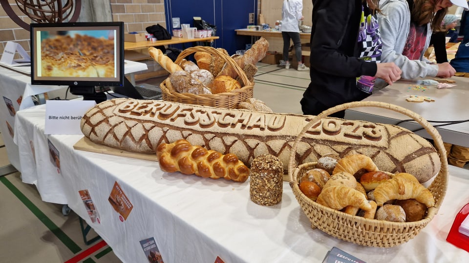 Grosses Brot mit Aufschrift «Berufsschau 2023», davor ein Zopf und Körbe mit Backwaren.