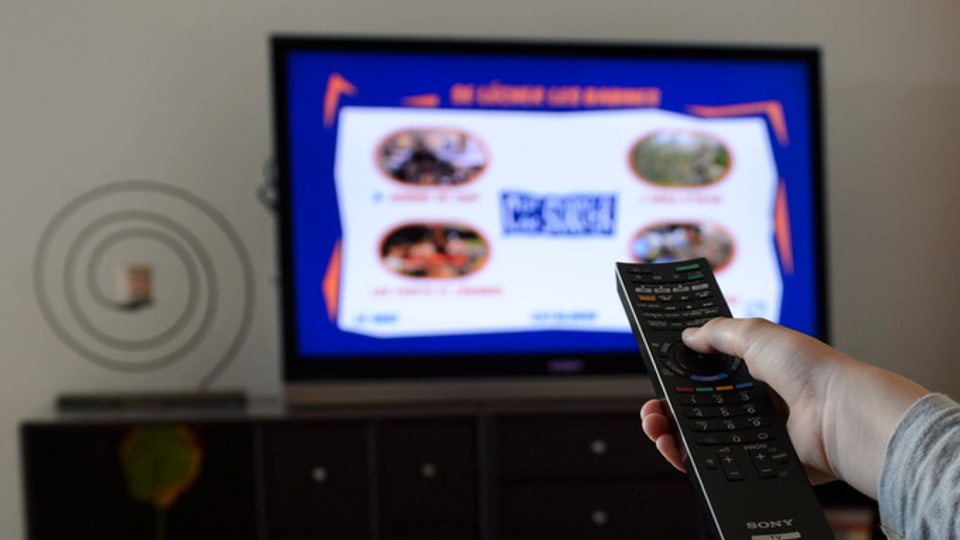 In maun che tegn il telecumond d'ina televisiun.