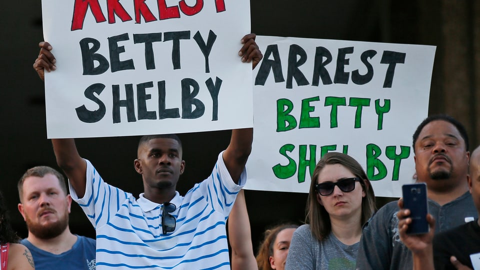 Protestas a Tulsa suenter ch'in afroamerican era vegnì sajettà giu entras ina policista. Plirs demonstrants tegnan enta maun placats cun si: Arrest Betty Shelby