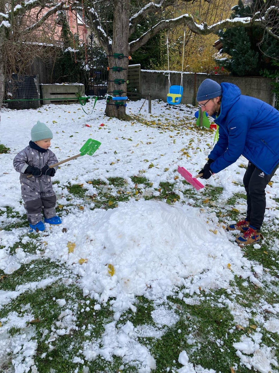Vater mit Kind im Garten am Schneeschaufeln