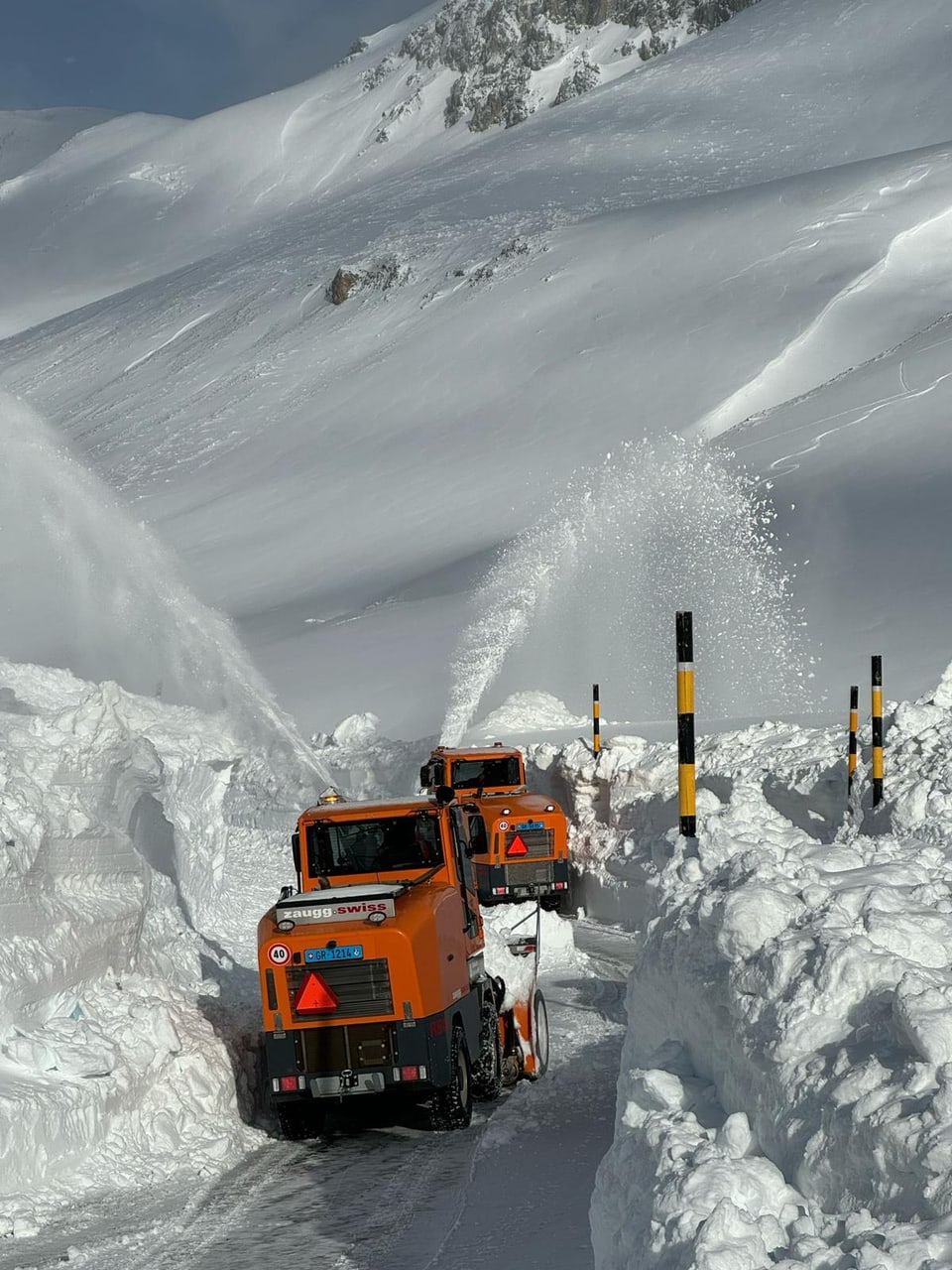 Schneeräumfahrzeuge räumen eine verschneite Bergstrasse.