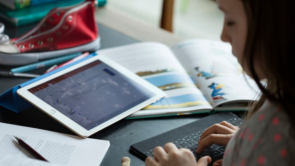 Uffant che fa lezias cun tablet e computer.
