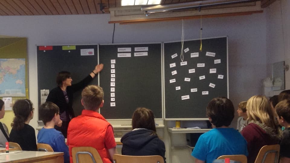 Ina classa da scola rumantscha durant l'instrucziun da franzos. La scolasta mussa insatge alla tavla.