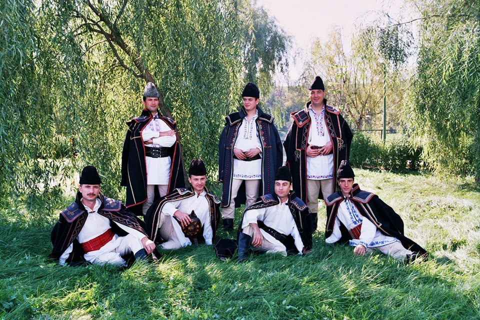 7 Männer in rumänischer Tracht posieren auf einer Wiese