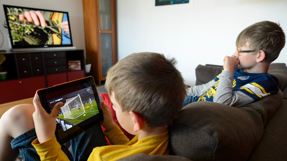 Purtret da dus uffants che guardan televisiun. 