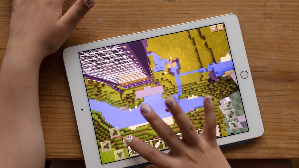 Ina mattetta dat in gieu sin in iPad - ins vesa mo l'iPad ed ils mauns pitschens cun unglas coluradas.
