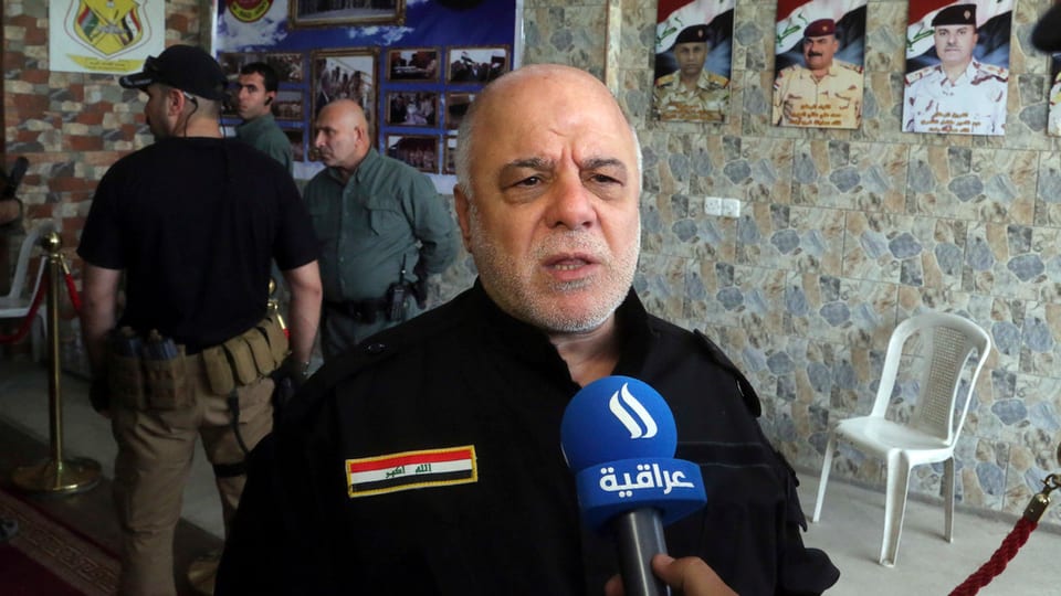 Al-Abadi en ina chasa, discurrind en il microfon.