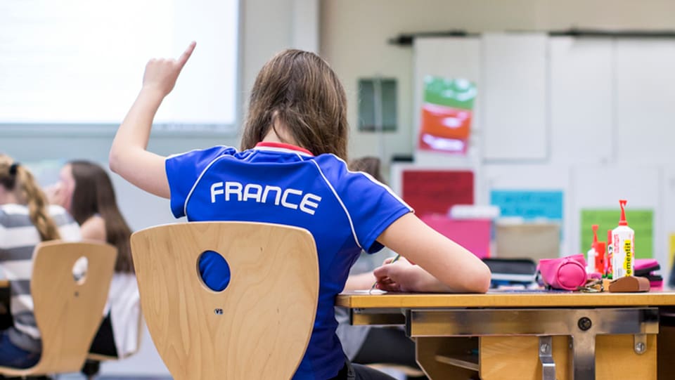 Ina scolara cun in T-Shirt blau e l'inscripziun France sesa en in baun da scola e tegn si il det.