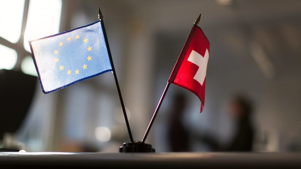 Bandierinas da l'UE e da la Svizra sin ina maisa.