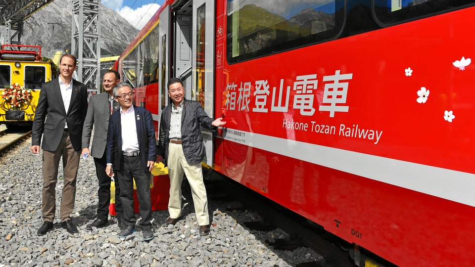 Il directur da la viafier retica Renato Fasciati, il president Stefan Engler e dus represchentants da las viafiers Hakone Tozan stattan avant in car da la viafier retica cotschen. Sin quel è scrit si en letra giapunaisas hakone Tozan Railway. Plinavant entgins maletgs da flurs (sihlouettas alvas)