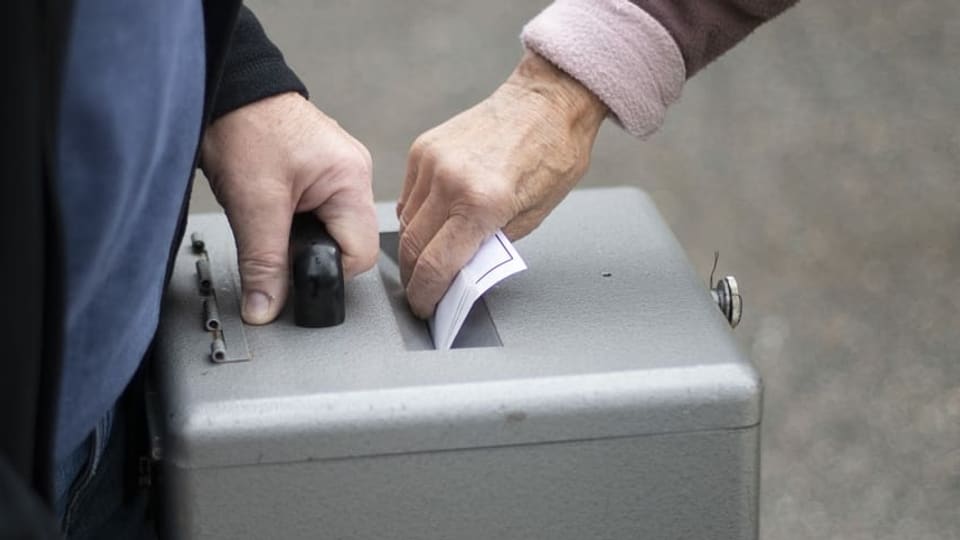 Purtret d'ina urna ed ina dunna che bitta en la brev da votaziun. 