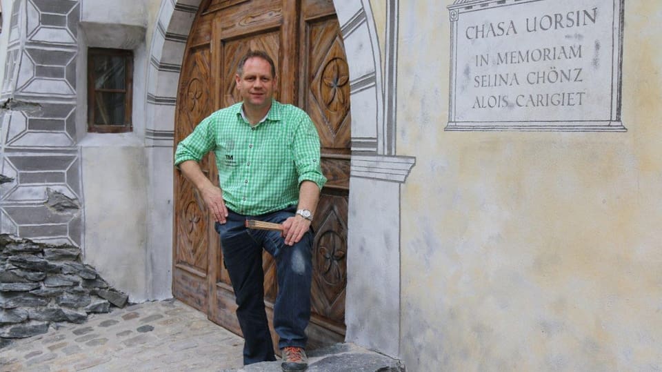 in scrinari cun chamischa verda e jeans stat avant ina chasa engiadinaisa